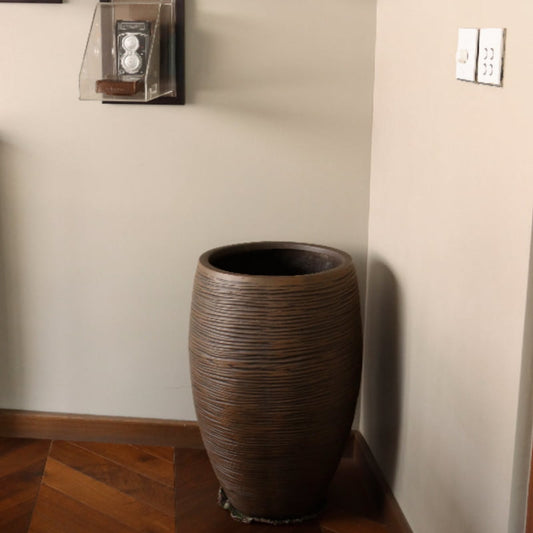 Inside the house, on a wood floor the Dark Brown Dual Tone Wood Rib High, a round tall textured luxury planter made from FRP you can buy online at Sukham Home, a sustainable furniture, gardening and home decor store in Kolkata, India