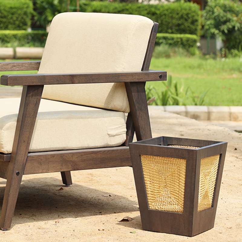 Placed outdoors, next to the Poise Armchairs, the Ash Grey Pile Paper Bin, a waste paper bin made from golden grass that you can buy online at Sukham Home, a sustainable furniture, kitchen & dining and home decor store in Kolkata, India