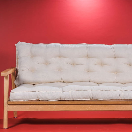 Against a red background, the Pearly Oak Antique Poise Sofa, a wooden cushioned midcentury sofa you can buy online at Sukham Home, a sustainable furniture, kitchen & dining and home decor store in Kolkata, India