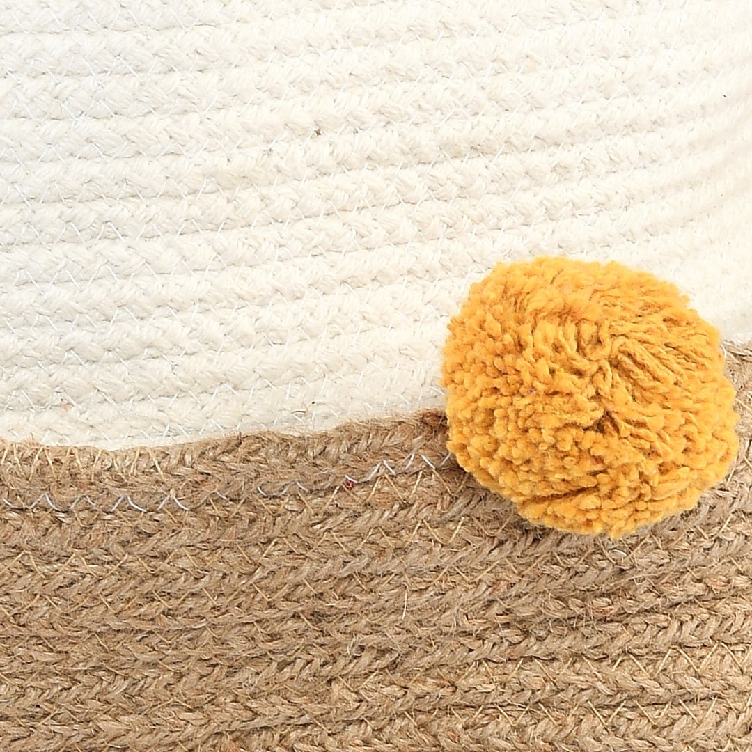 Close up of the yellow pom pom on the Playful Pom Pom Basket Set, a set of 2 yellow and white jute & cotton baskets you can buy online at Sukham Home, a sustainable furniture, kitchen & dining and home decor store in Kolkata, India