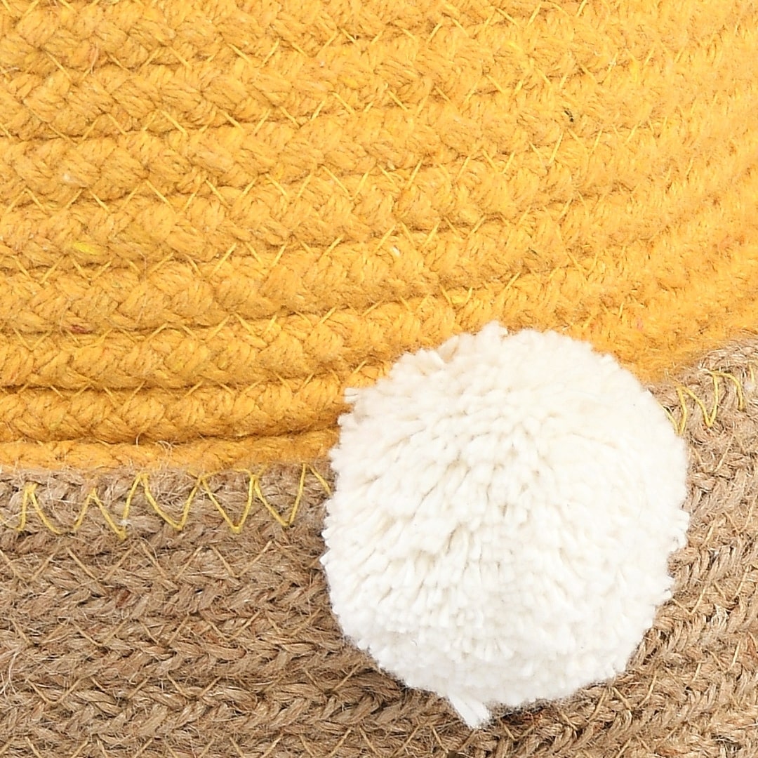 Close up of the white pom pom on the Playful Pom Pom Basket Set, a set of 2 yellow and white jute & cotton baskets you can buy online at Sukham Home, a sustainable furniture, kitchen & dining and home decor store in Kolkata, India