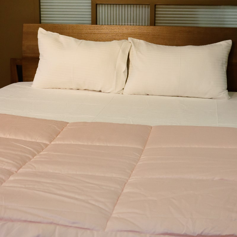 Placed on a bed, the White Sateen Striped Bedsheet, a king and queen size cotton bedsheet you can buy online at Sukham Home, a sustainable furniture, gardening and home decor store in Kolkata, India