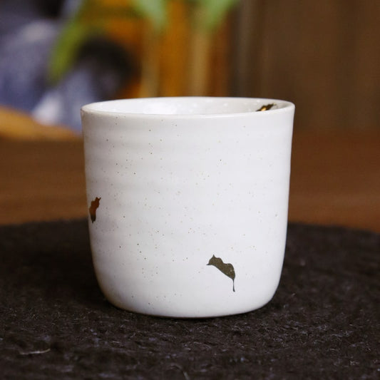 On a black table mat, the Ivory Ganga Kulhad, an pure white and 24-karat gold ceramic cup/glass you can buy online at Sukham Home, a sustainable furniture, gardening and home decor store in Kolkata, India