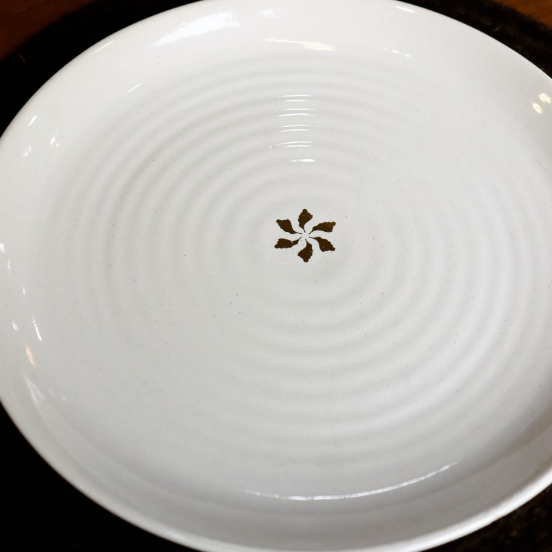 Placed on a black table mat, Ivory Ganga Dinner Plate, a pure white and 24-karat gold ceramic plate you can buy online at Sukham Home, a sustainable furniture, gardening and home decor store in Kolkata, India