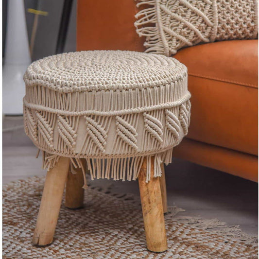 Placed on a carpet, the Alabaster Macrame Stool, a white ottoman made from cotton and mango wood, available at Sukham Home, a sustainable furniture, kitchen & dining and home decor store in Kolkata, India
