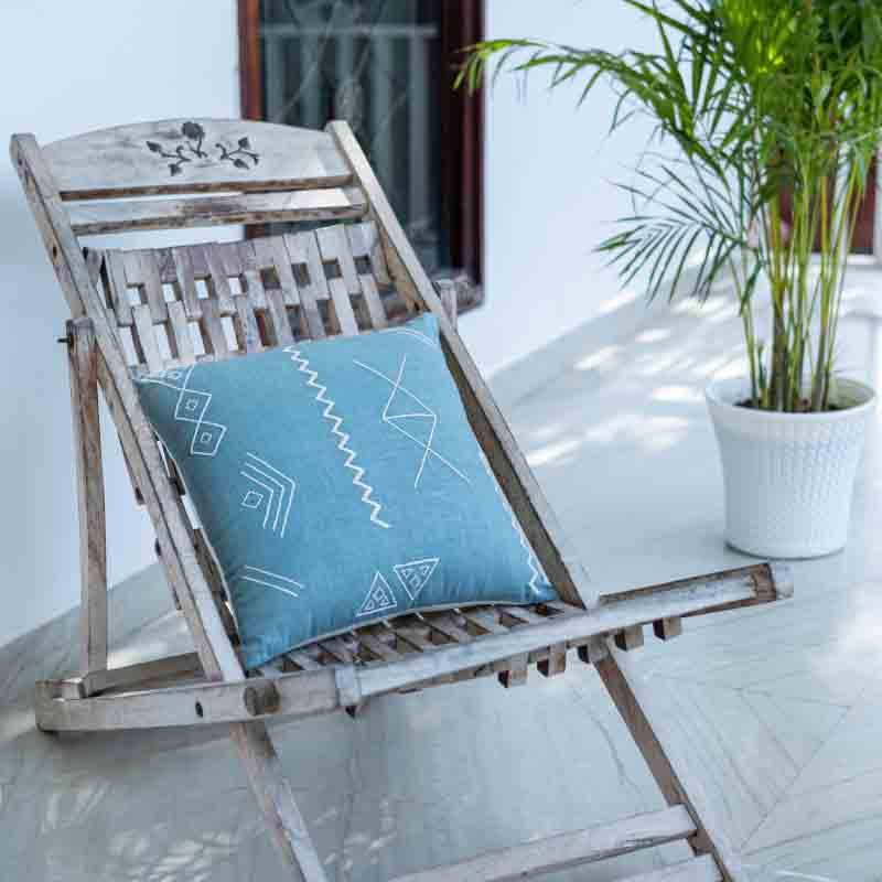 The Blue Grotto Cushion, a square accent pillow in a cerulean blue colour with graceful embroidery in an outdoor setting you can buy online at Sukham Home, a sustainable furniture, kitchen & dining and home decor store in Kolkata, India.