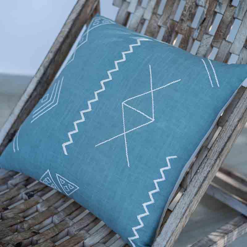 An side angle view of the Blue Grotto Cushion, a square accent pillow in a cerulean blue colour with graceful embroidery you can buy online at Sukham Home, a sustainable furniture, kitchen & dining and home decor store in Kolkata, India.