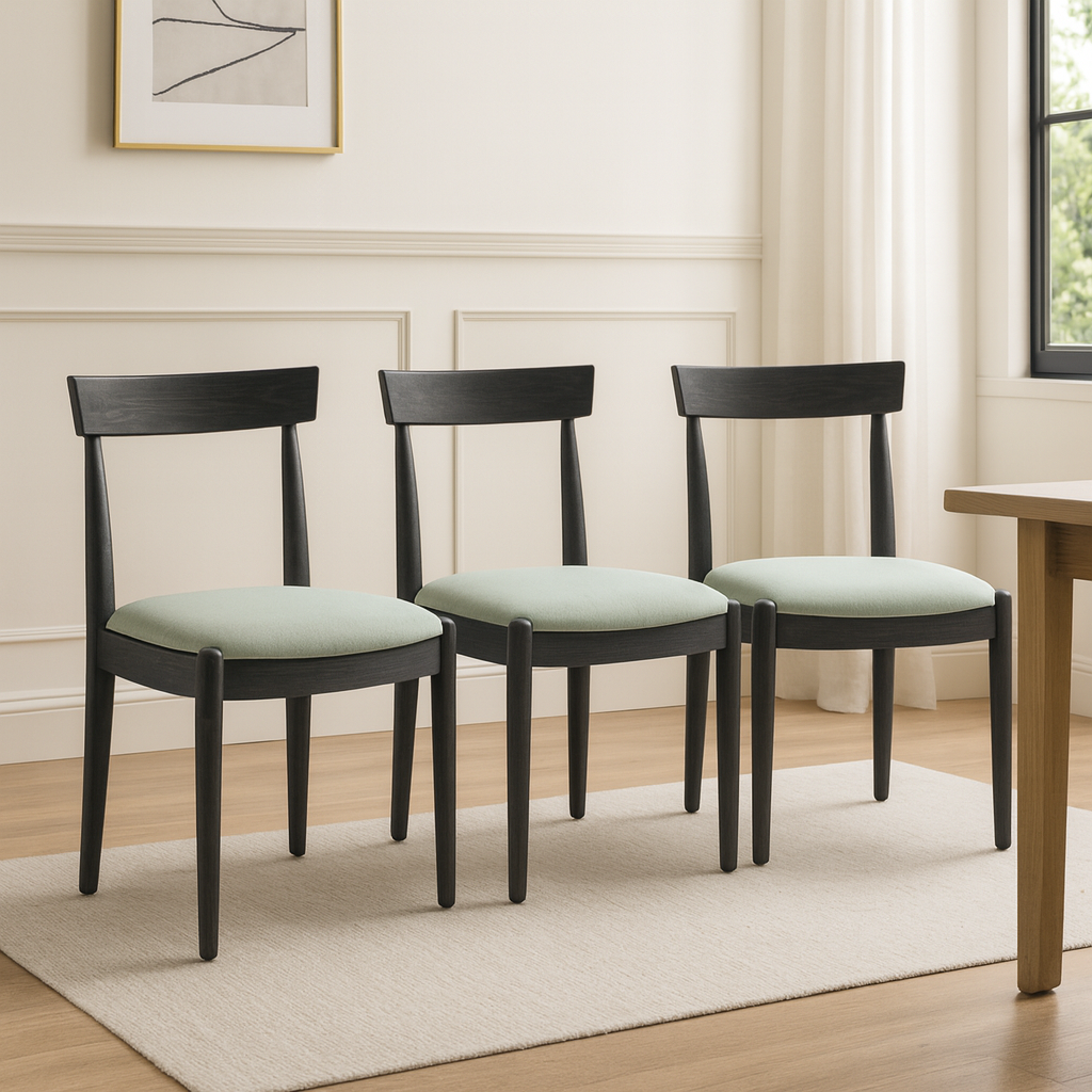 Three Ash Charcoal Bow Dining Chairs with light green padded cushions in a room with a wooden table and framed artwork on the wall.