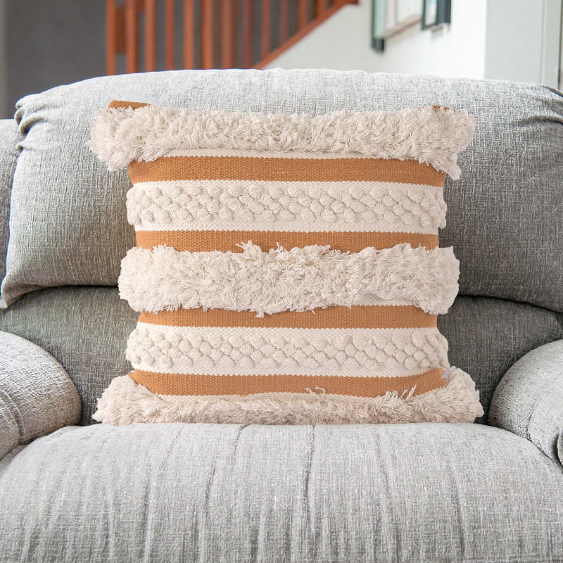 Placed on a sofa is the Chunky Hazelnut Cushion, a square accent pillow with fringes and knots and a delightful yellow tone which you can buy online at Sukham Home, a sustainable furniture, kitchen & dining and home decor store in Kolkata, India.