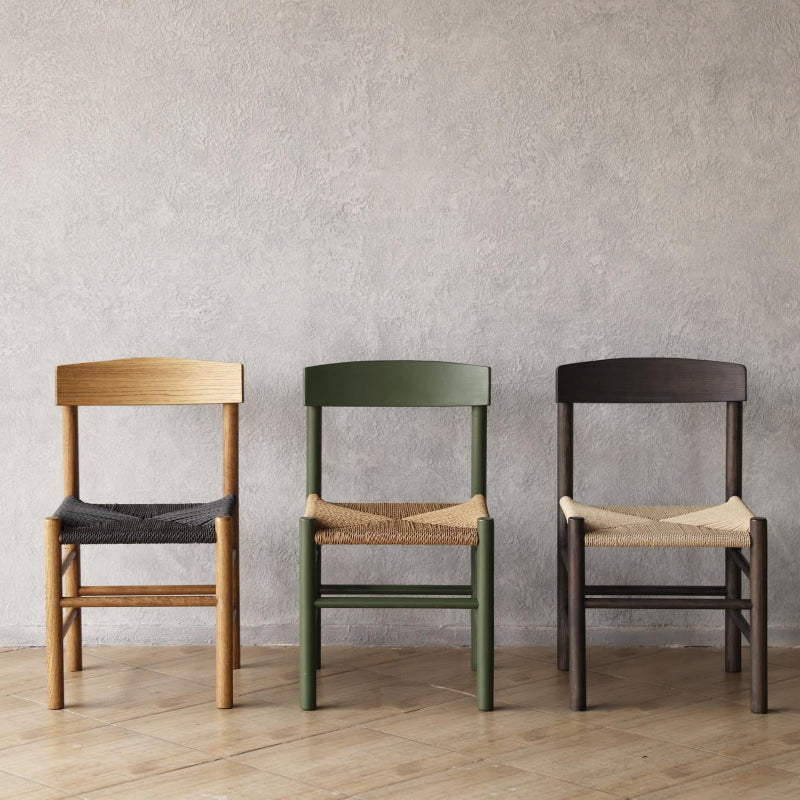 Three wooden People's chairs with different finishes against a plain wall.