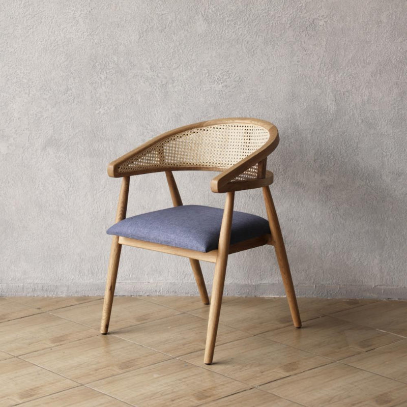 Wooden Pie Chair with wicker backrest and blue cushion against a gray wall.