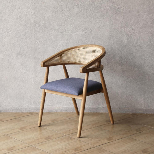 Wooden Pie Chair with wicker backrest and blue cushion against a gray wall.