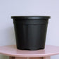 Placed on a table, 10 inch black nursery pot and gardening tools you can buy online at Sukham Home, a sustainable furniture, gardening and home decor store in Kolkata, India