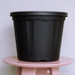 Placed on a pink table, the 14 inch black nursery pot and gardening tools you can buy online at Sukham Home, a sustainable furniture, gardening and home decor store in Kolkata, India