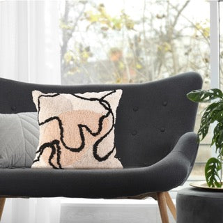 Arranged on a dark charcoal sofa, the Art-Inspired Tufted Cushion, a square pink, grey, white and black accent pillow available at Sukham Home, a sustainable furniture, kitchen & dining and home decor store in Kolkata, India