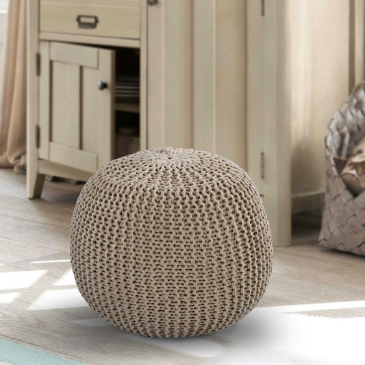 On a wooden floor, the Beige Knitted Pouf, an sandy brown ottoman made from cotton, available at Sukham Home, a sustainable furniture, kitchen & dining and home decor store in Kolkata, India