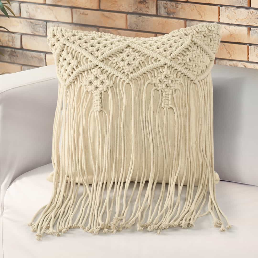 Arranged on a grey sofa, the Beige White Macrame Cushion with Fringes, a square accent pillow you can buy online at Sukham Home, a sustainable furniture, kitchen & dining and home decor store in Kolkata, India