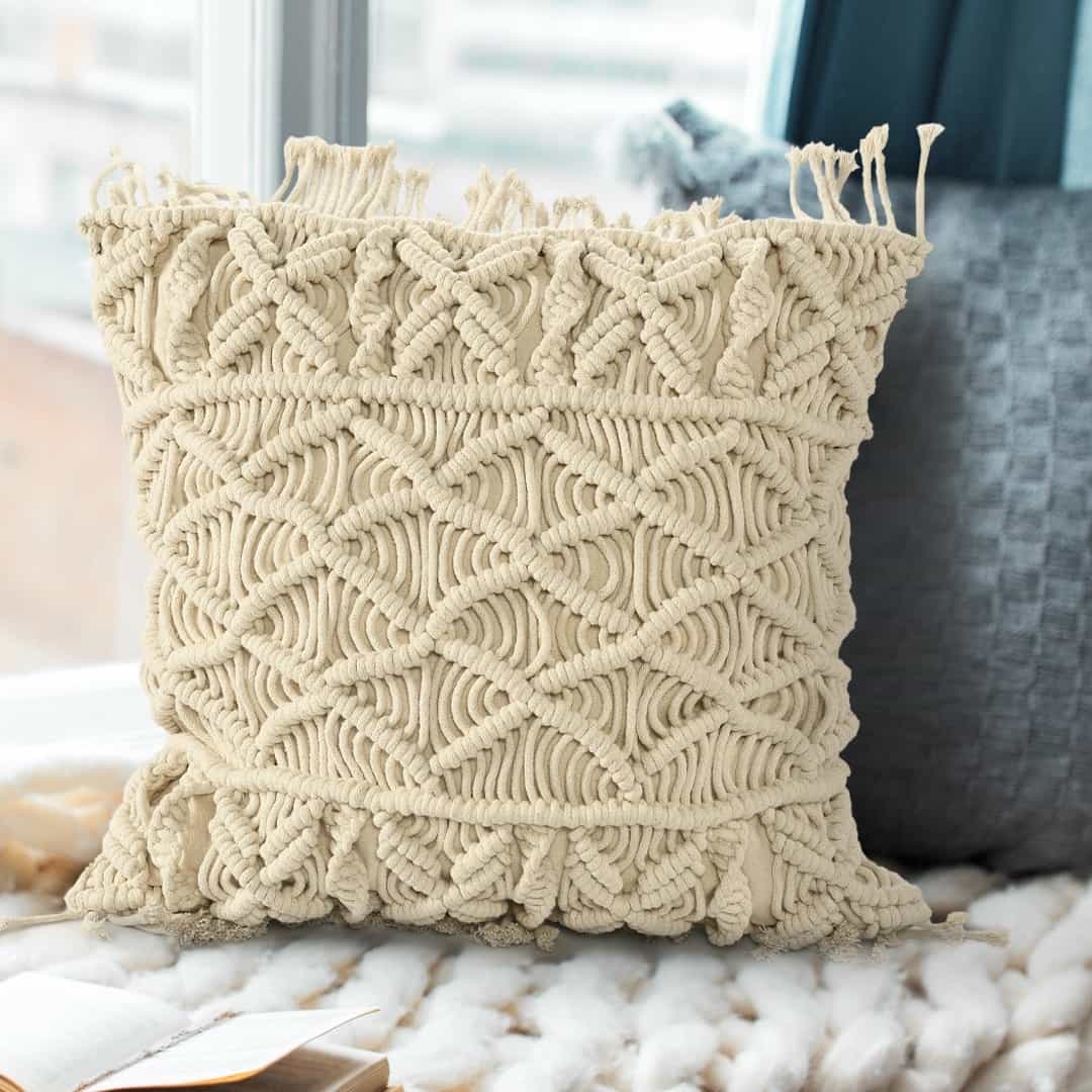 Arranged in a room, the Beige White Macrame Cushion, a square accent pillow you can buy online at Sukham Home, a sustainable furniture, kitchen & dining and home decor store in Kolkata, India