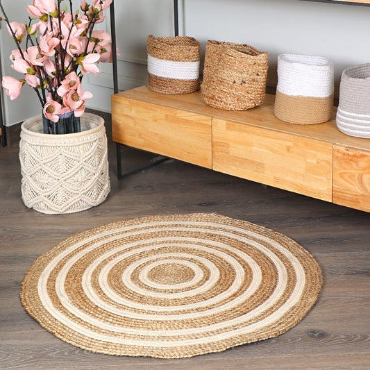 On a wooden floor, the Round Jute Rug, a circular jute and white cotton carpet you can buy online at Sukham Home, a sustainable furniture, kitchen & dining and home decor store in Kolkata, India