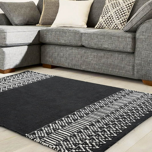 Arranged under a grey sofa, the Woven Black and White Rug, a rectangle cotton carpet in black & white you can buy online at Sukham Home, a sustainable furniture, kitchen & dining and home decor store in Kolkata, India