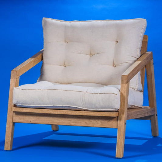 Against a blue background, the Oak Natural with Umber fabric, the Bliss Armchair, a wooden cushioned midcentury seat you can buy online at Sukham Home, a sustainable furniture, kitchen & dining and home decor store in Kolkata, India