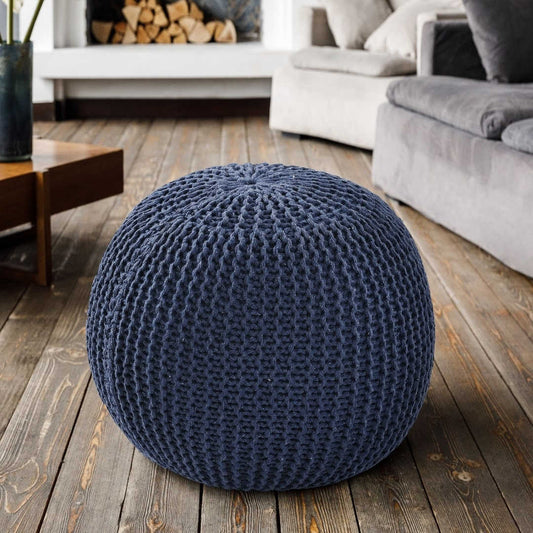 On a wooden floor, the Blue Knitted Pouf, a navy blue ottoman made from cotton, available at Sukham Home, a sustainable furniture, kitchen & dining and home decor store in Kolkata, India