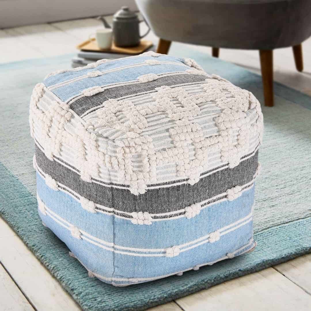 Placed on a carpet near an armchair, the Geometric Details Blue Pouf, an ottoman made from cotton, available at Sukham Home, a sustainable furniture, kitchen & dining and home decor store in Kolkata, India