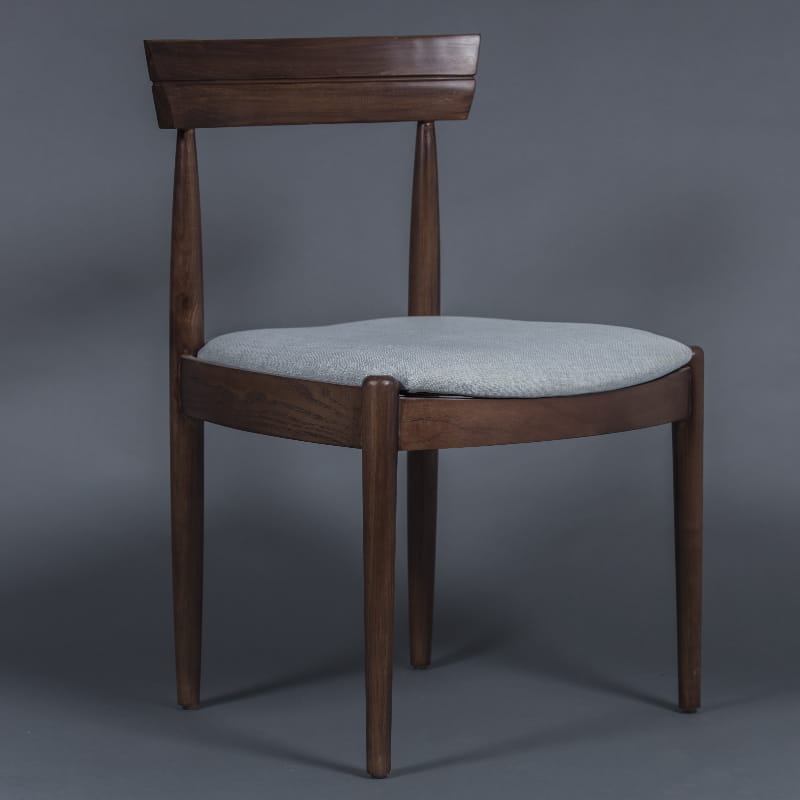 Against a grey background, the Bow, a solid wood chair with a padded cushion seat you can buy online at Sukham Home, a sustainable furniture and home decor store in Kolkata, India