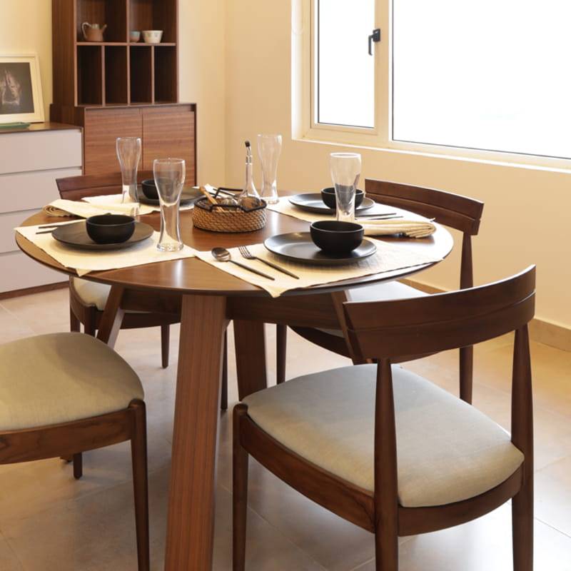 Full Moon Dining Table with the Walnut Natural Bow, a solid wood chair with a padded cushion seat you can buy online at Sukham Home, a sustainable furniture and home decor store in Kolkata, India