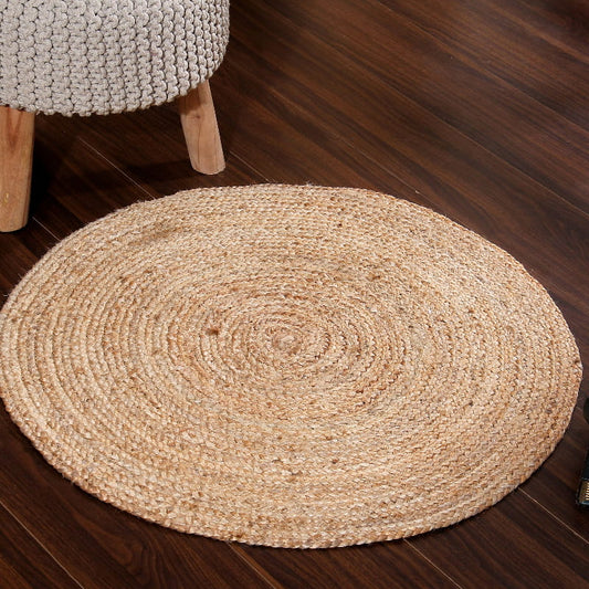 On a wooden floor, the Braided Round Jute Rug, a circular jute carpet you can buy online at Sukham Home, a sustainable furniture, kitchen & dining and home decor store in Kolkata, India