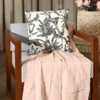 Placed on a blue chair, the Call of the Wild Cushion, a square white and grey jungle-printed accent pillow available at Sukham Home, a sustainable furniture, kitchen & dining and home decor store in Kolkata, India