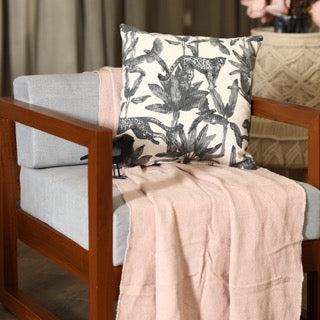 Arranged on an armchair, the Call of the Wild Cushion, a square white and grey jungle-printed accent pillow available at Sukham Home, a sustainable furniture, kitchen & dining and home decor store in Kolkata, India