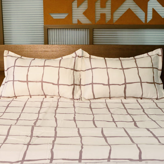 Front view, placed on a bed the Chequered Snow White Printed Bedsheet, a white and mauve king size cotton bedsheet you can buy online at Sukham Home, a sustainable furniture, gardening and home decor store in Kolkata, India