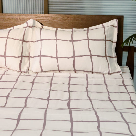 One pillowcase and bedsheet of the Chequered Snow White Printed Bedsheet, a white and mauve king size cotton bedsheet you can buy online at Sukham Home, a sustainable furniture, gardening and home decor store in Kolkata, India