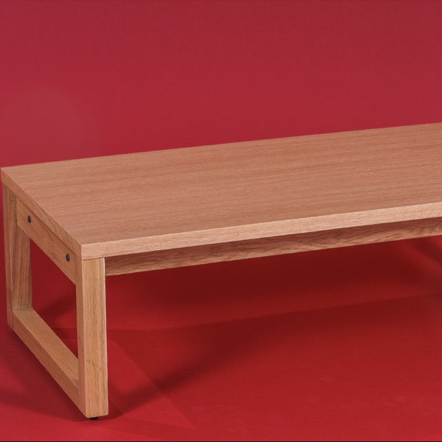 Against a red background, close up of the Oak Natural Core Centre Table, a wooden coffee and centre table you can buy online at Sukham Home, a sustainable furniture, kitchen & dining and home decor store in Kolkata, India
