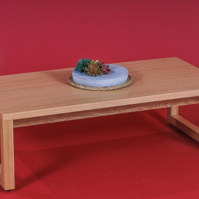 Against a red background, with table decor placed on top of it, the Core Centre Table, a wooden coffee and centre table you can buy online at Sukham Home, a sustainable furniture, kitchen & dining and home decor store in Kolkata, India