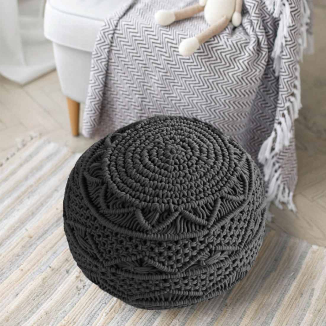 Placed on a rug, the Dark Grey Macrame Pouf, a grey ottoman made from cotton, available at Sukham Home, a sustainable furniture, kitchen & dining and home decor store in Kolkata, India