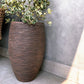 On a rooftop terrace, the Dark Brown Dual Tone Wood Rib High, a round tall textured luxury planter made from FRP you can buy online at Sukham Home, a sustainable furniture, gardening and home decor store in Kolkata, India