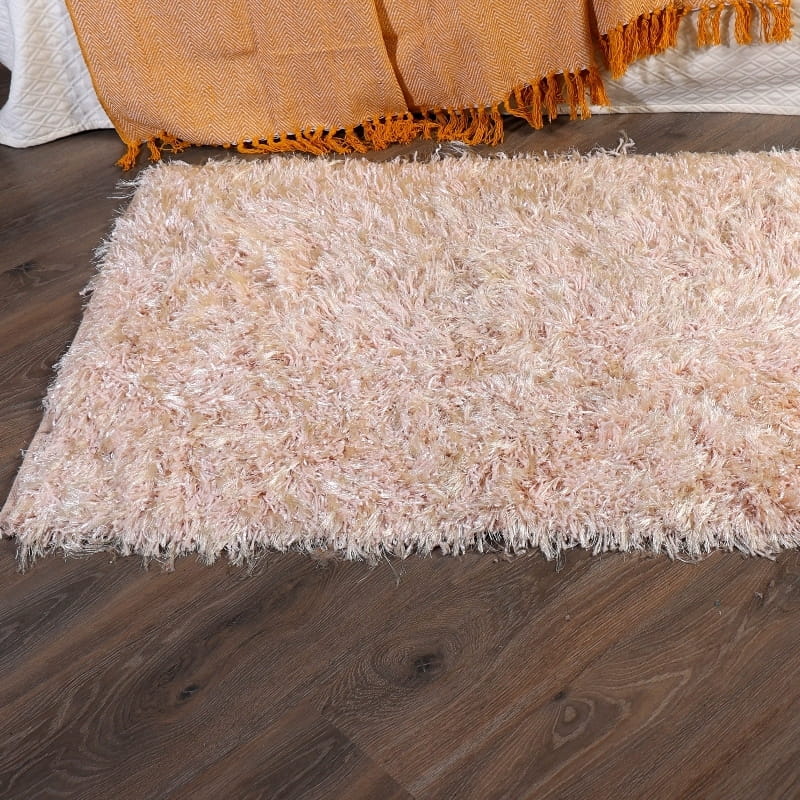 Under a bed on a wooden floor, the Dori Shag Rug, a rectangle shaggy cotton carpet in pale pink you can buy online at Sukham Home, a sustainable furniture, kitchen & dining and home decor store in Kolkata, India