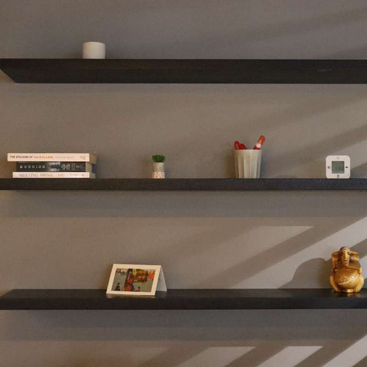 Against a beige wall, the Ash Grey Float Shelf, a multipurpose wooden wall shelf and storage solution you can buy online at Sukham Home, a sustainable furniture, kitchen & dining and home decor store in Kolkata, India