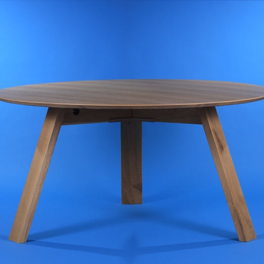 Against a blue background, the Oak Antique Full Moon Dining Table, a wooden 4 and 6-seater round dining table you can buy online at Sukham Home, a sustainable furniture, kitchen & dining and home decor store in Kolkata, India