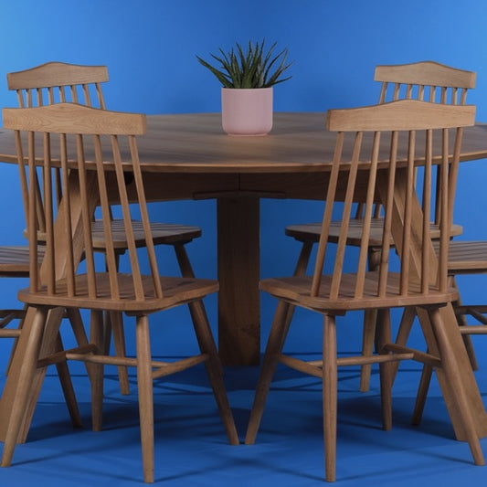 Against a blue background, with the String Chairs, the Oak Antique Full Moon Dining Table, a wooden 4 and 6-seater round dining table you can buy online at Sukham Home, a sustainable furniture, kitchen & dining and home decor store in Kolkata, India