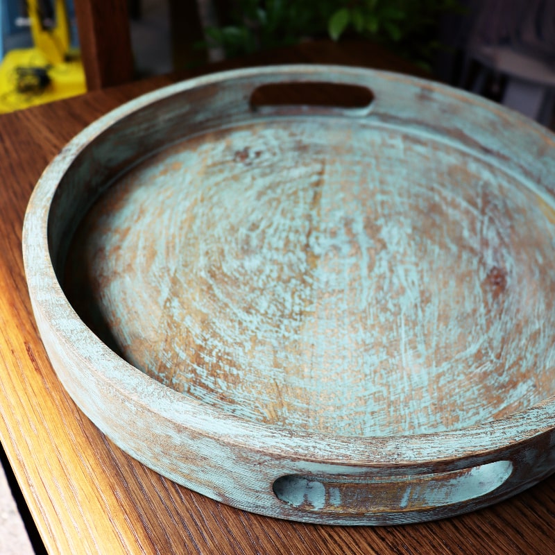 Against a wooden table, the Gangtok Sage Wooden Tray, a solid wood patina green platter and serve ware you can buy online at Sukham Home, a sustainable furniture, kitchen & dining and home decor store in Kolkata, India