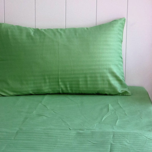 A single pillowcase and sheet from the Green Sateen Striped Bedsheet, a king size cotton bedsheet you can buy online at Sukham Home, a sustainable furniture, gardening and home decor store in Kolkata, India