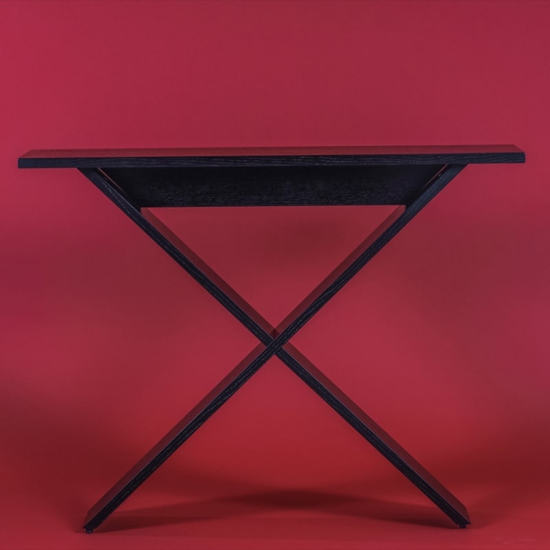 Against a red background, the Ash Charcoal Greet, a wooden entryway console you can buy online at Sukham Home, a sustainable furniture, kitchen & dining and home decor store in Kolkata, India