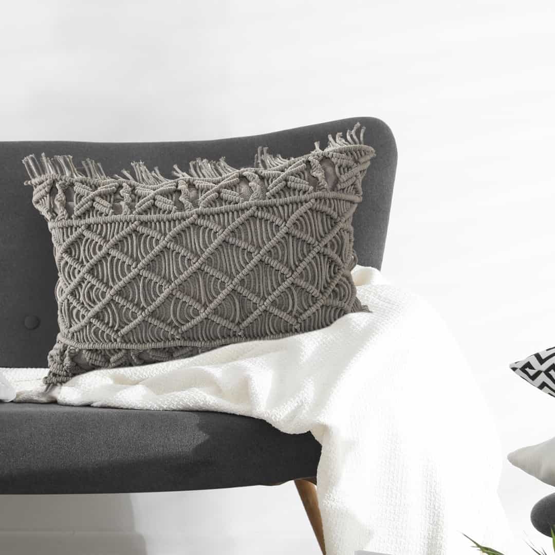 Arranged in a room, the Grey Macrame Cushion, a rectangle accent pillow you can buy online at Sukham Home, a sustainable furniture, kitchen & dining and home decor store in Kolkata, India