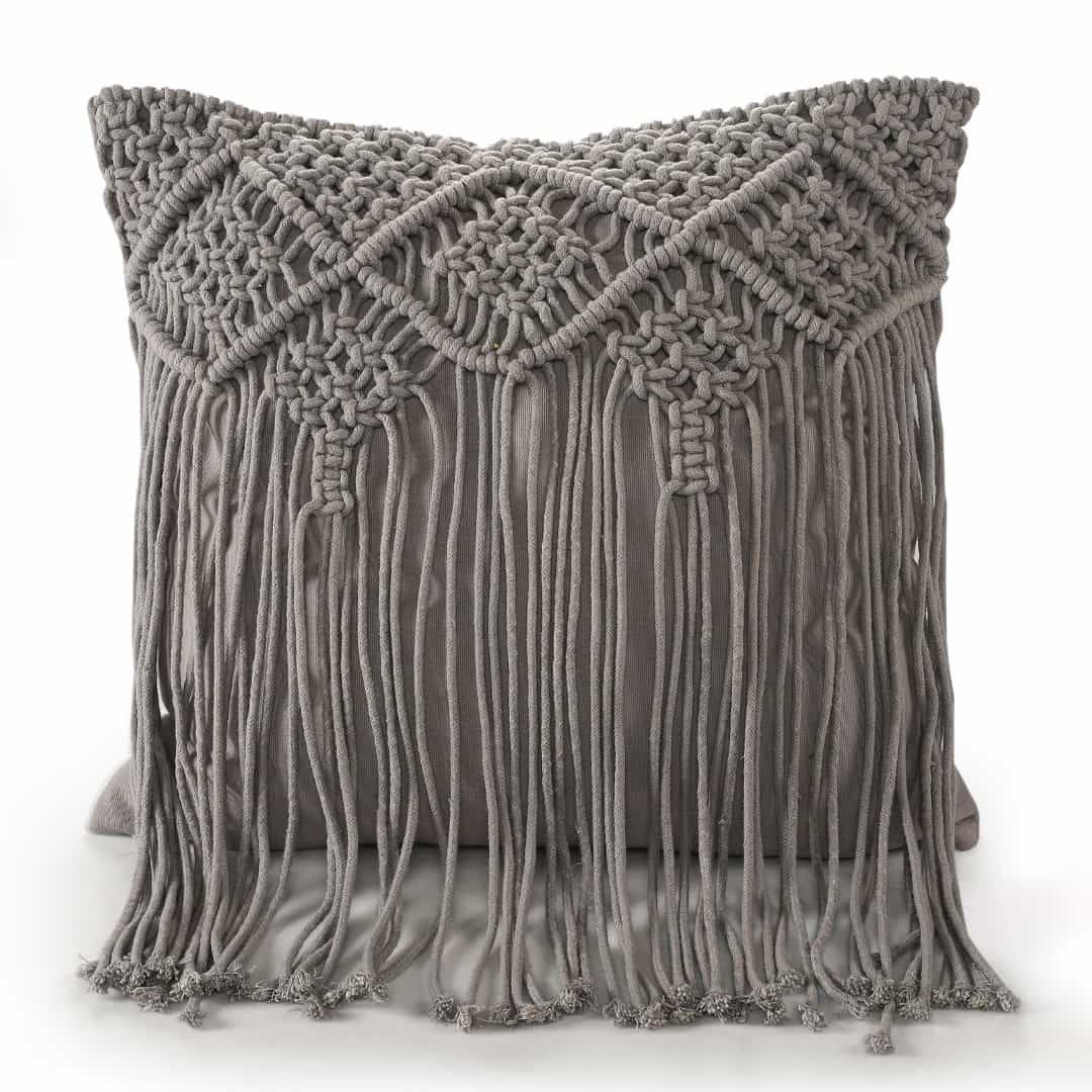 Against of a white background, the Grey Macrame Cushion with Fringes, a square accent pillow you can buy online at Sukham Home, a sustainable furniture, kitchen & dining and home decor store in Kolkata, India