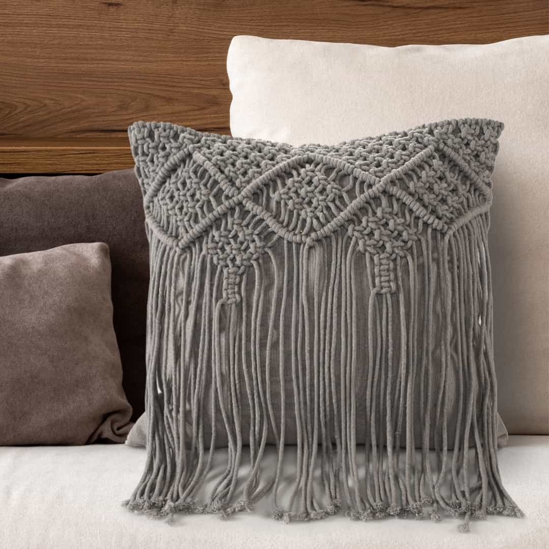 Arranged in a room, the Grey Macrame Cushion with Fringes, a square accent pillow you can buy online at Sukham Home, a sustainable furniture, kitchen & dining and home decor store in Kolkata, India