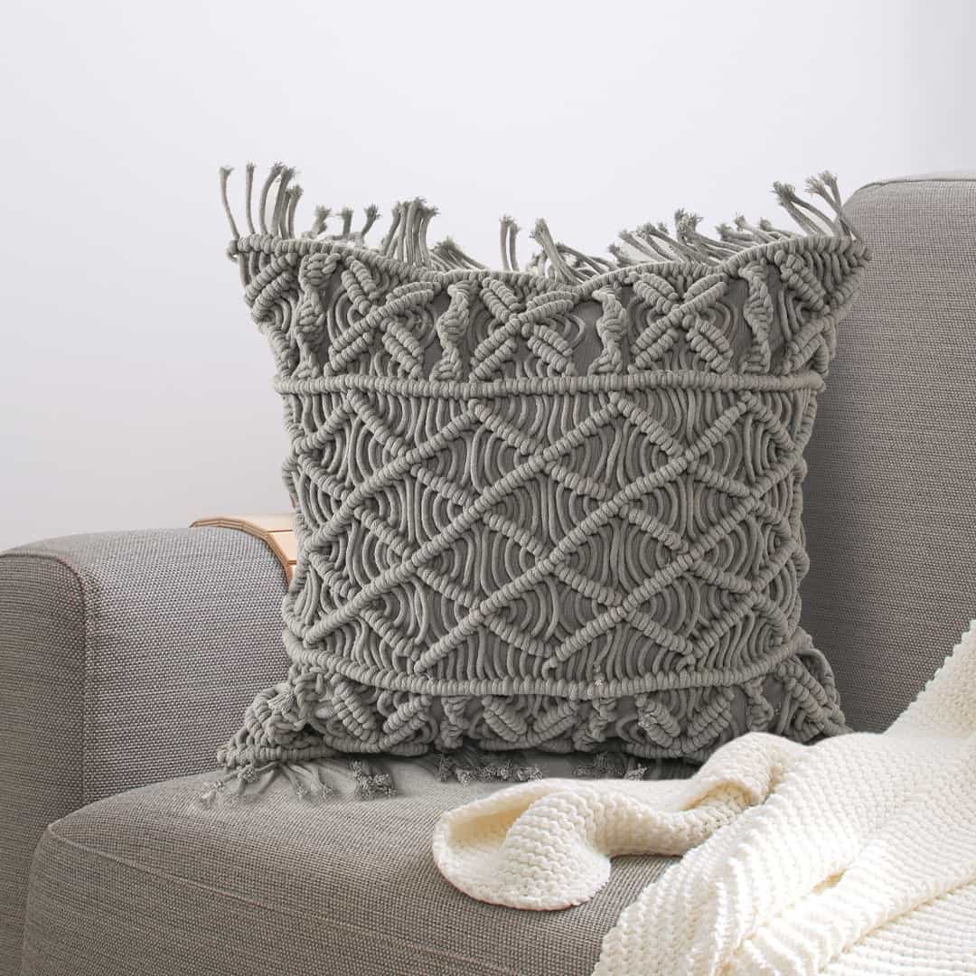 Arranged on a grey sofa, the Grey Macrame Cushion, a square accent pillow you can buy online at Sukham Home, a sustainable furniture, kitchen & dining and home decor store in Kolkata, India