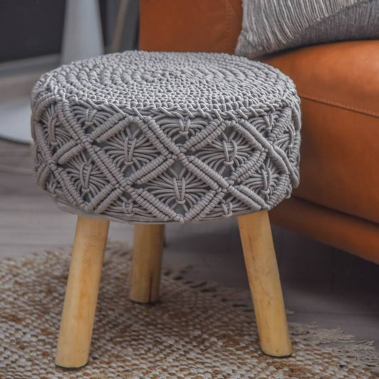 Placed on a carpet, the Grey Macrame Stool, a grey ottoman made from cotton and mango wood, available at Sukham Home, a sustainable furniture, kitchen & dining and home decor store in Kolkata, India